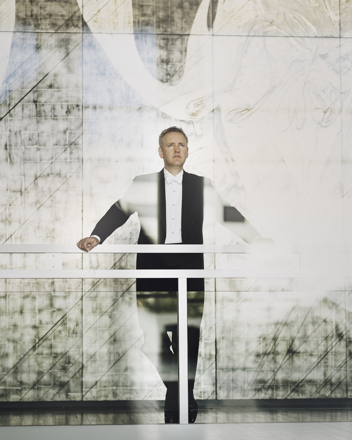 Michael Francis in white tie and tails at a glass balustrade before a pale mural