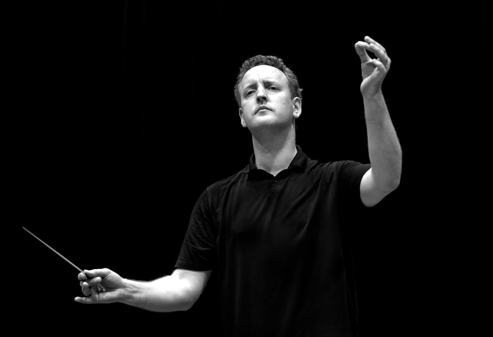 Michael Francis conducting against a black background, arm raised