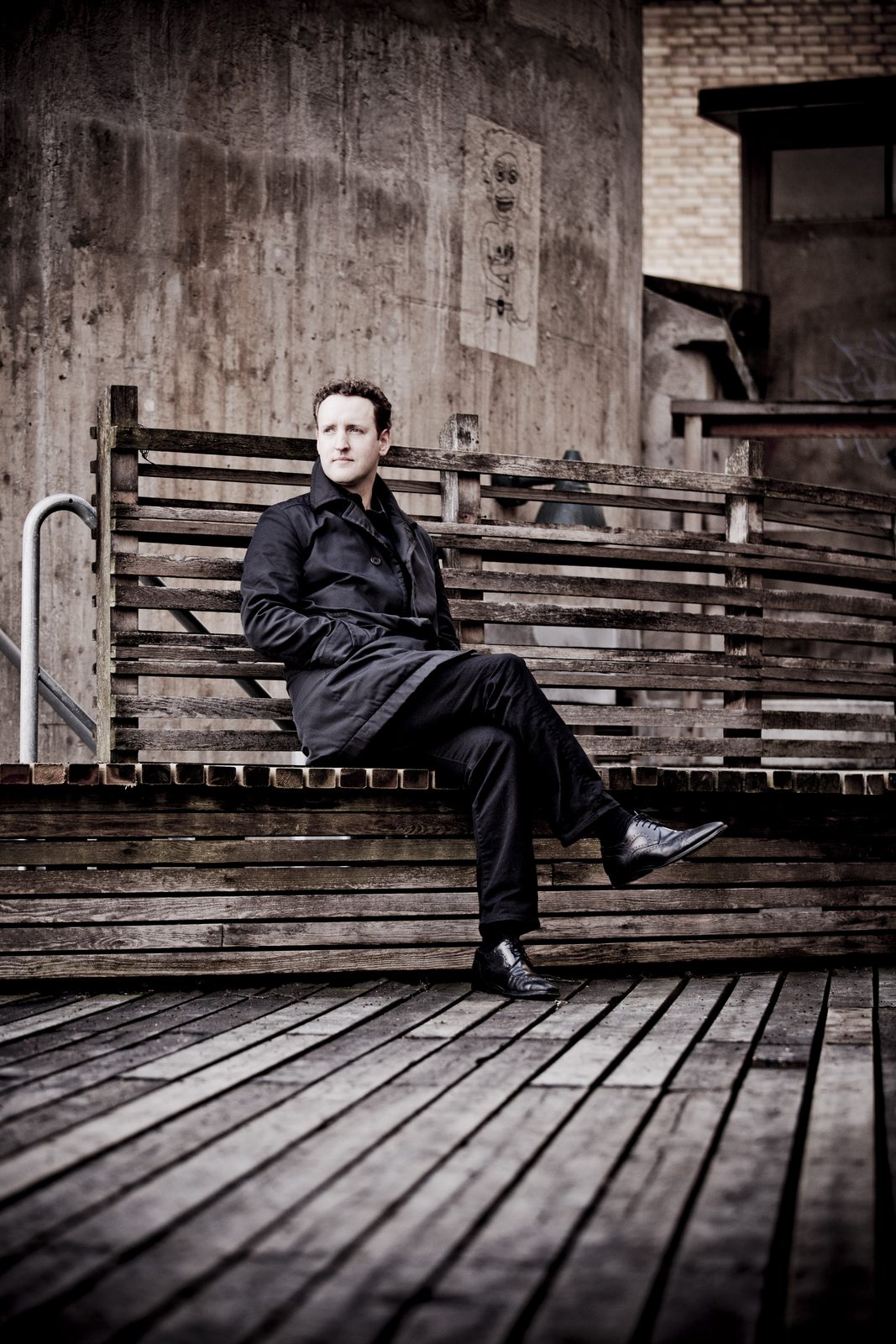 Michael Francis seated on a wooden bench in a dark coat