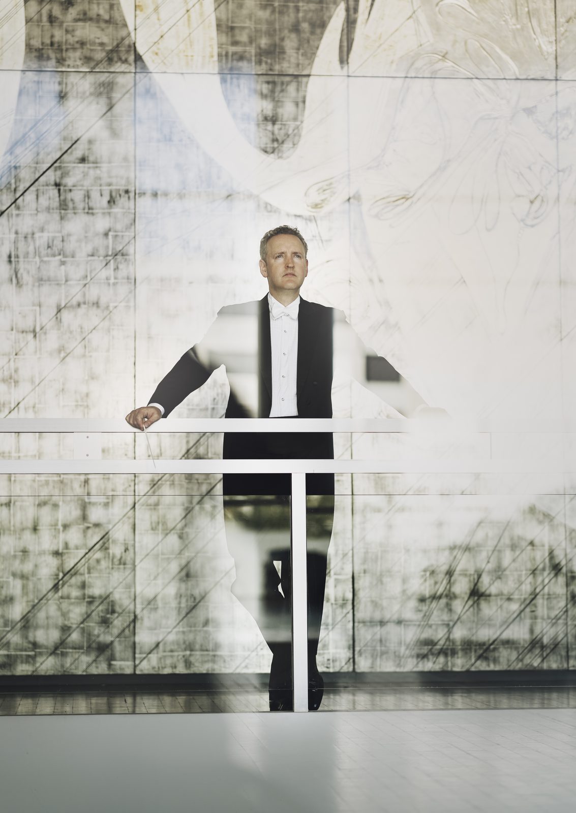 Michael Francis in tails at a glass balustrade before a pale mural