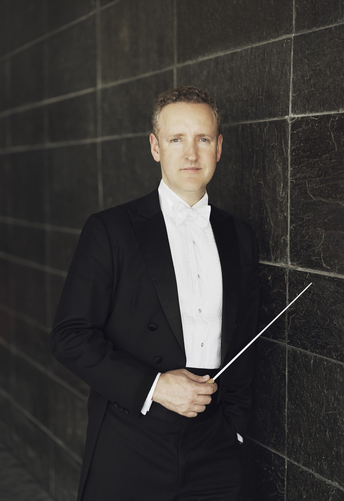 Michael Francis in white tie and tails against a dark tiled wall