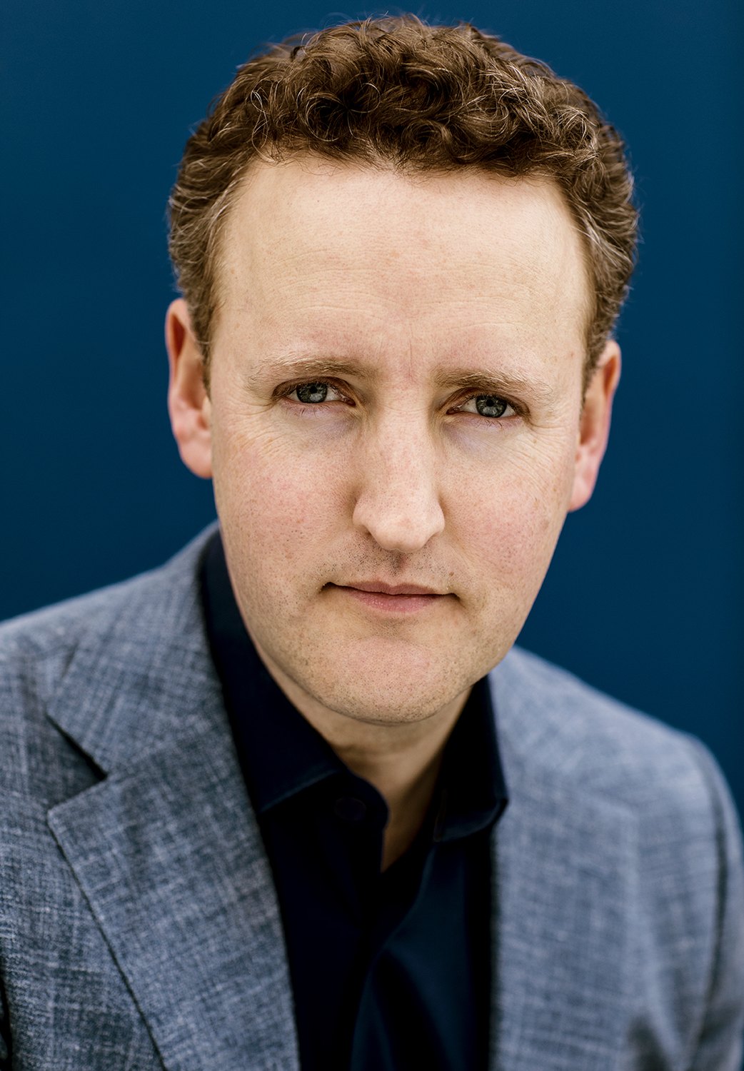 Colour portrait of Michael Francis in a grey blazer against a blue background